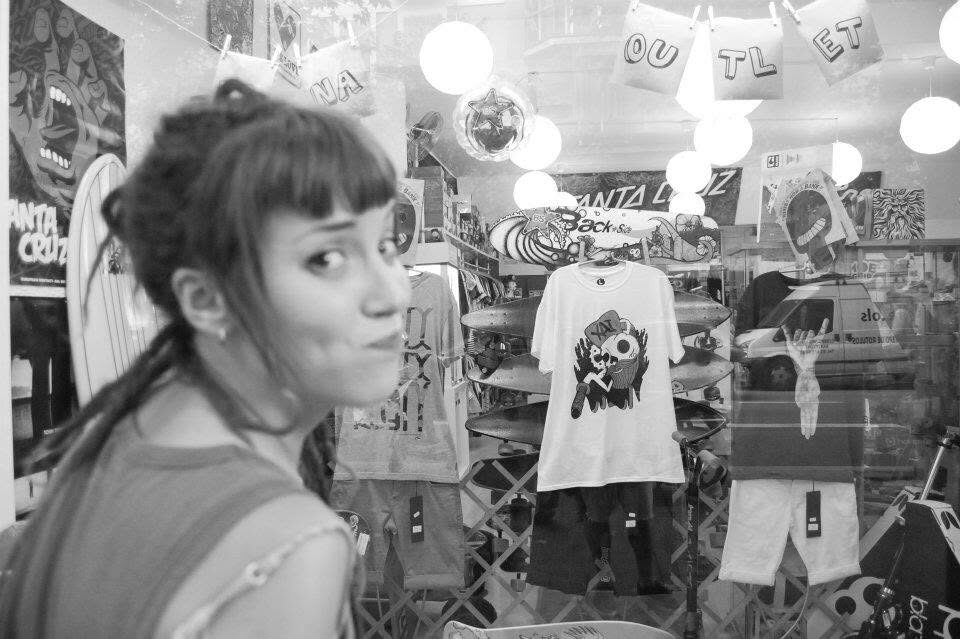 Black and white photo of a girl in the shop, XAI shirts displayed on the wall behind her