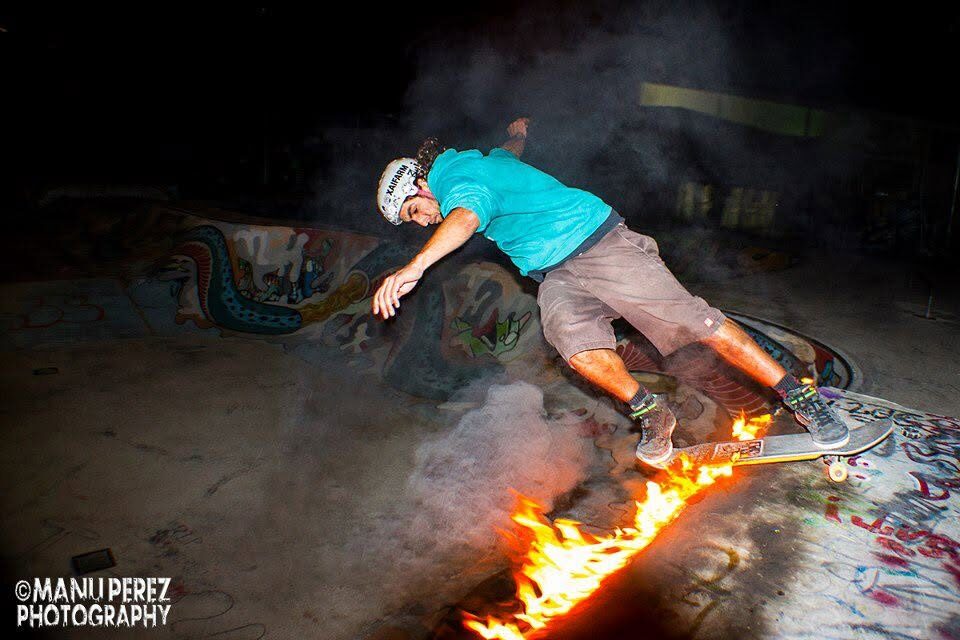 A skateboarder riding a graffitied ramp with a fire burning in the foreground