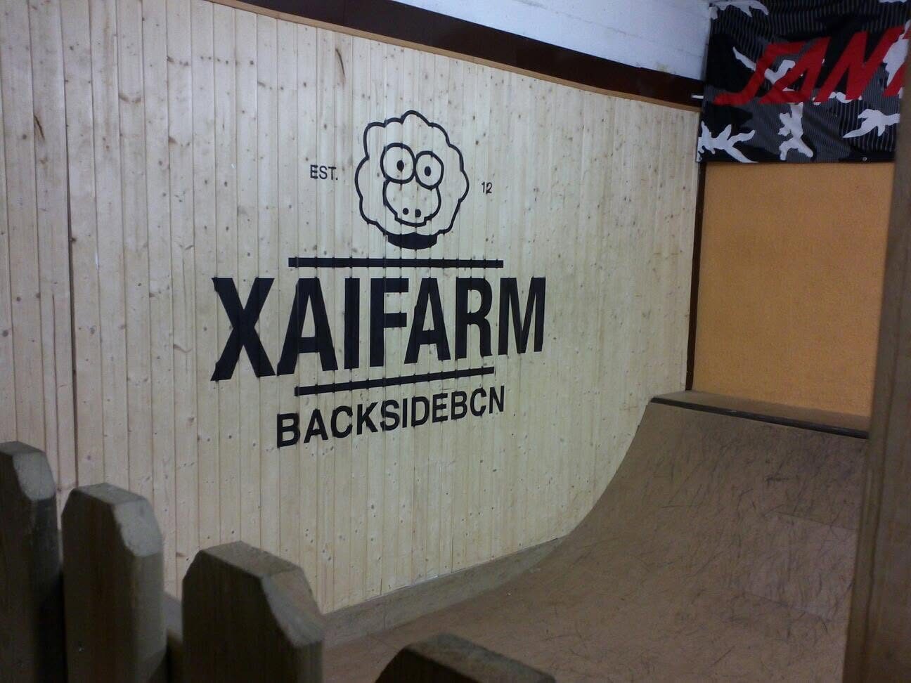 The inside of XAI FARM: a timber mini ramp against a wall painted with the sheep logo and XAIFARM BACKSIDEBCN
