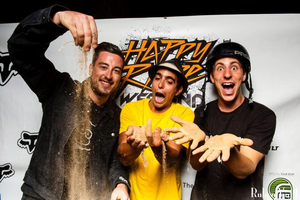 Three riders messing around in front of an event photocall backdrop covered in sponsor logos