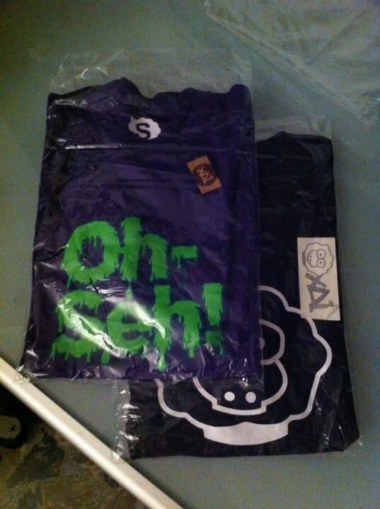 Two bagged t-shirts with swing tags: a purple Oh Sh! print and a sheep graphic