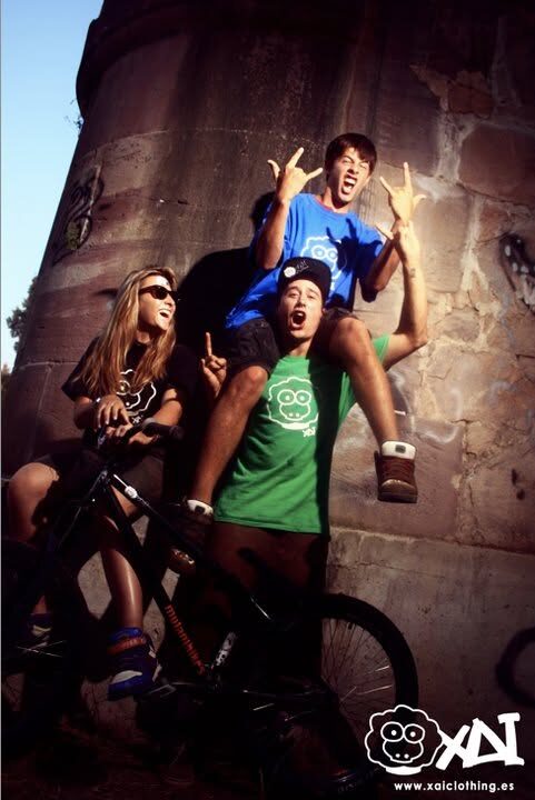 Three friends posing on a concrete wall, with www.xaiclothing.es printed in the corner