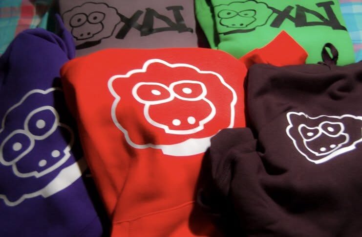 Folded hoodies in purple, red, green and brown, each with a sheep print