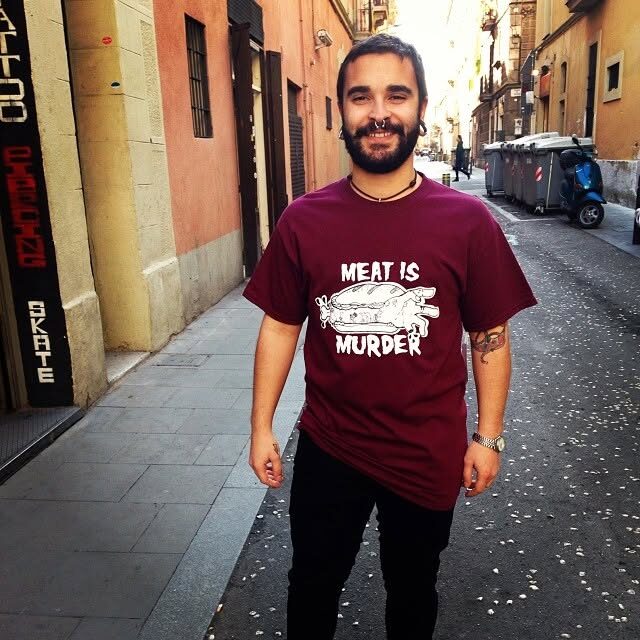 A man in a dark red MEAT IS MURDER t-shirt in a narrow Barcelona street